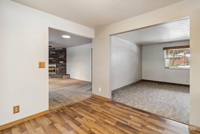 carpeted empty room featuring a fireplace, wood finished floors, and baseboards