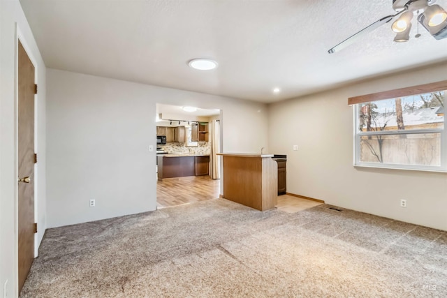 kitchen with backsplash, a kitchen island, black microwave, light countertops, and light colored carpet