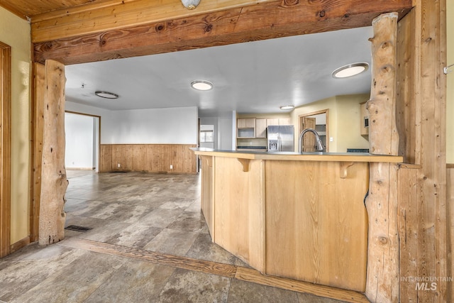 kitchen with wood walls, kitchen peninsula, a kitchen breakfast bar, light brown cabinets, and stainless steel fridge