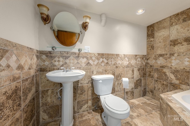 bathroom with tile walls, a bathtub, and toilet