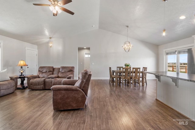 living room with ceiling fan with notable chandelier, vaulted ceiling, baseboards, and dark wood-style flooring