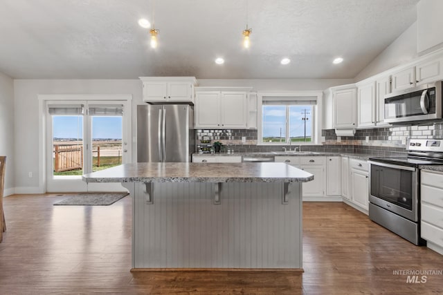 kitchen featuring lofted ceiling, stainless steel appliances, a sink, a center island, and decorative backsplash