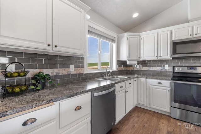 kitchen featuring white cabinets, lofted ceiling, dark wood-style floors, stainless steel appliances, and a sink