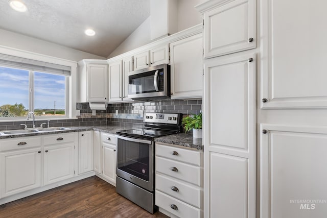 kitchen with vaulted ceiling, a sink, decorative backsplash, stainless steel appliances, and white cabinetry