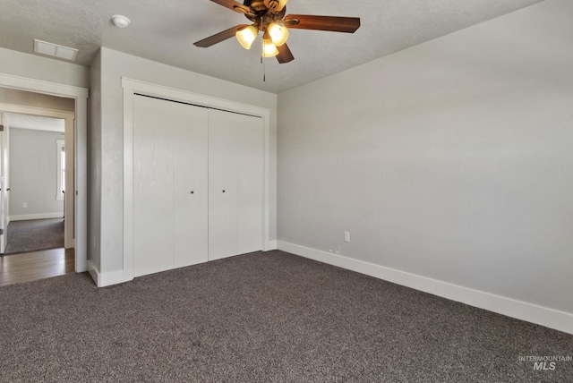 unfurnished bedroom featuring visible vents, dark colored carpet, baseboards, and a closet