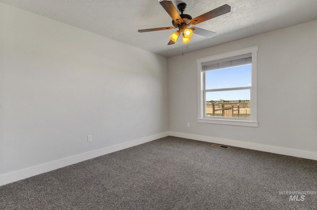 spare room with dark colored carpet, visible vents, a ceiling fan, baseboards, and a textured ceiling