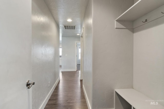 corridor featuring a textured ceiling, a textured wall, dark wood finished floors, baseboards, and visible vents