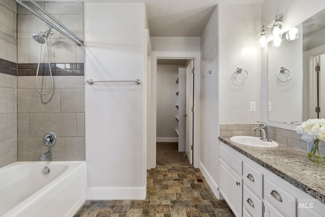 bathroom featuring stone finish flooring, baseboards, vanity, and washtub / shower combination