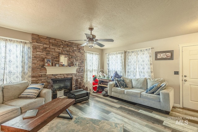 living room featuring ceiling fan, a textured ceiling, a stone fireplace, and hardwood / wood-style floors