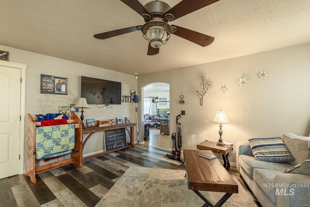 living room featuring ceiling fan, dark wood-type flooring, and a textured ceiling