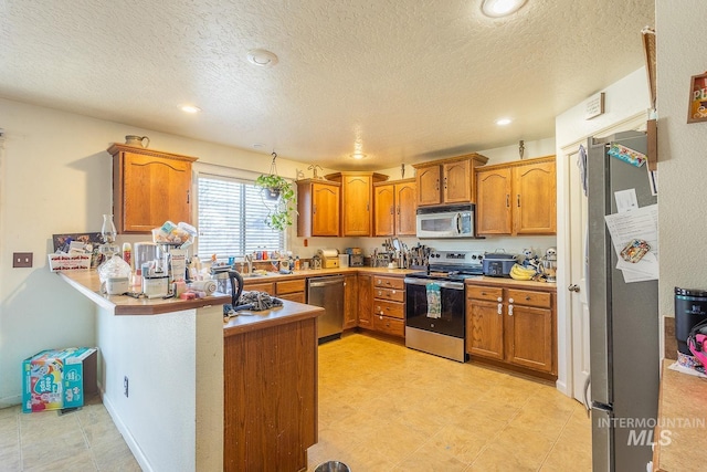 kitchen with sink, a textured ceiling, appliances with stainless steel finishes, and kitchen peninsula