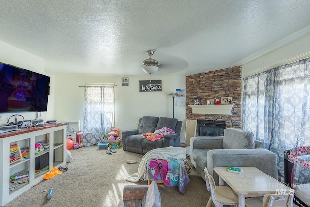 living room featuring ceiling fan, a textured ceiling, a stone fireplace, and carpet flooring