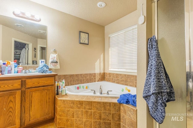 bathroom with a textured ceiling, tiled tub, and vanity