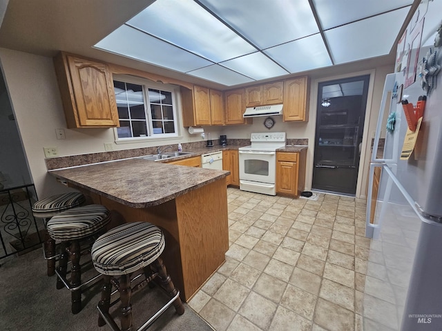 kitchen featuring dark countertops, white appliances, under cabinet range hood, and a peninsula