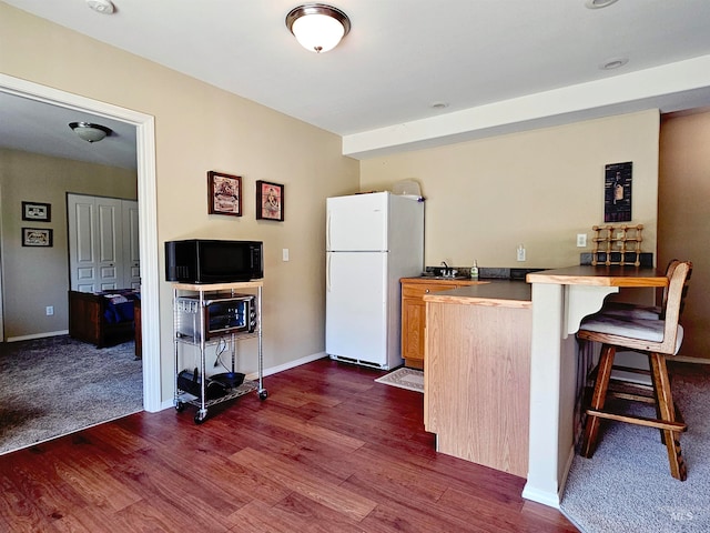 kitchen featuring a breakfast bar area, white fridge, dark hardwood / wood-style floors, and kitchen peninsula