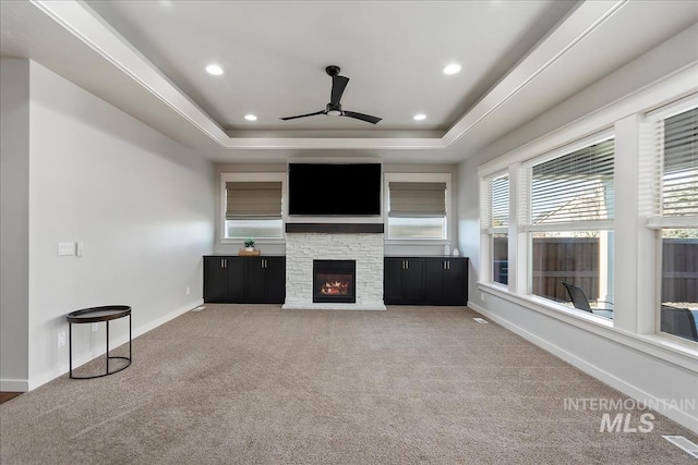 unfurnished living room with ceiling fan, carpet flooring, a fireplace, and a tray ceiling