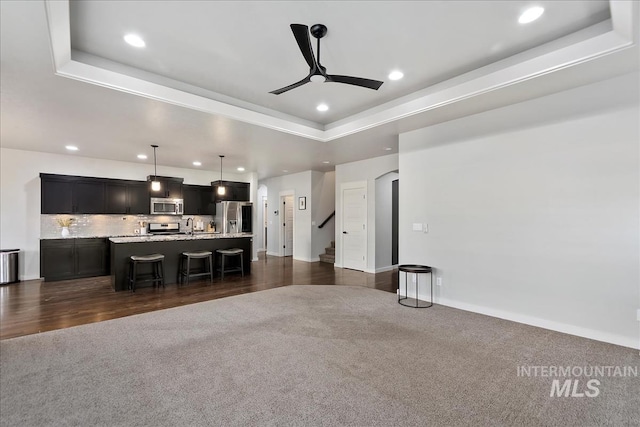 living room featuring ceiling fan, sink, a tray ceiling, and dark carpet