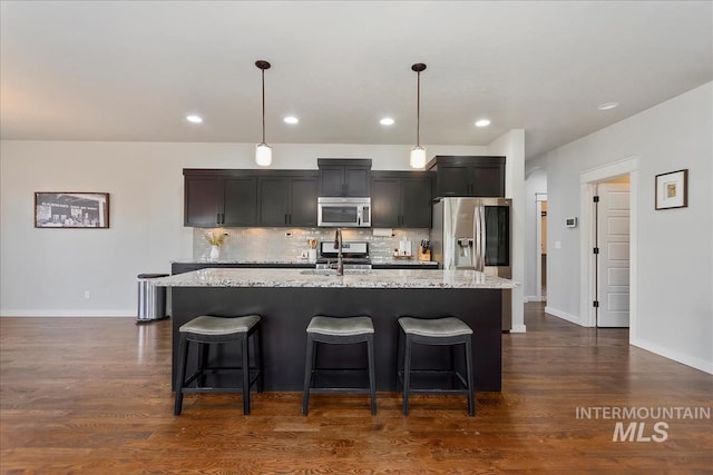 kitchen featuring appliances with stainless steel finishes, pendant lighting, sink, backsplash, and a center island with sink