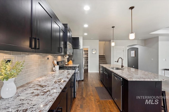 kitchen featuring pendant lighting, sink, stainless steel appliances, light stone countertops, and a center island with sink