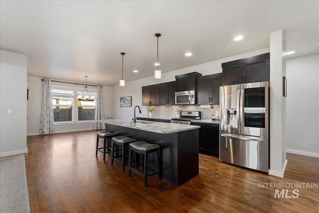 kitchen with sink, a kitchen island with sink, backsplash, stainless steel appliances, and a kitchen bar