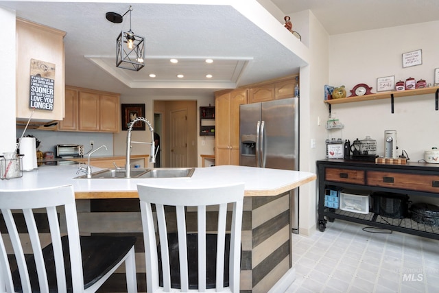 kitchen featuring light brown cabinetry, a peninsula, a tray ceiling, and a sink