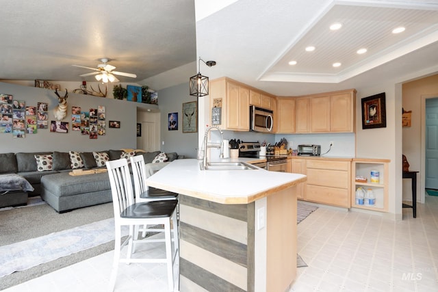 kitchen with a peninsula, a sink, stainless steel appliances, light brown cabinetry, and open floor plan