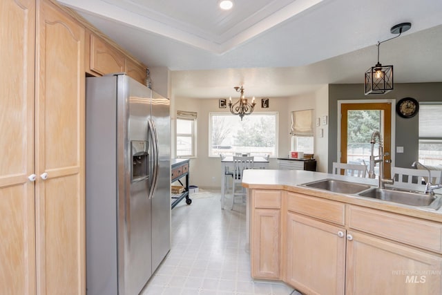 kitchen with light brown cabinets, a sink, pendant lighting, a raised ceiling, and stainless steel fridge