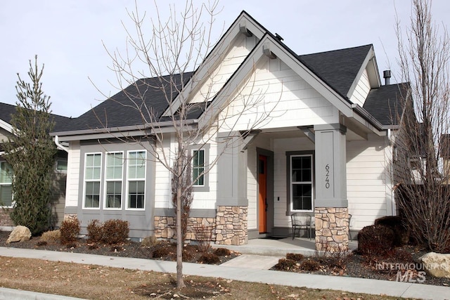 view of front of property featuring a porch, stone siding, and roof with shingles