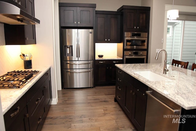 kitchen with light stone counters, wood finished floors, a sink, under cabinet range hood, and appliances with stainless steel finishes