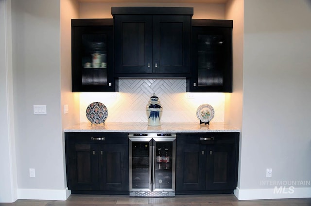 bar featuring a bar, wine cooler, baseboards, and backsplash