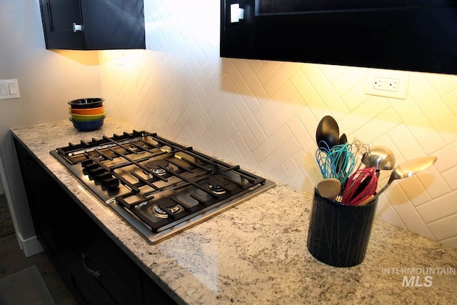 kitchen featuring light stone counters, dark cabinets, tasteful backsplash, and stainless steel gas stovetop