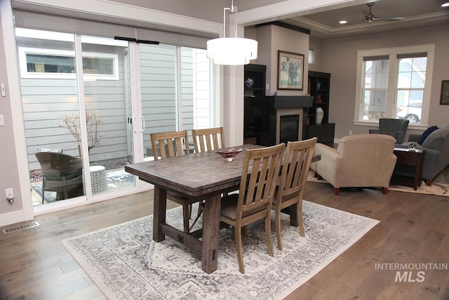 dining space featuring wood finished floors, visible vents, a tray ceiling, a glass covered fireplace, and crown molding