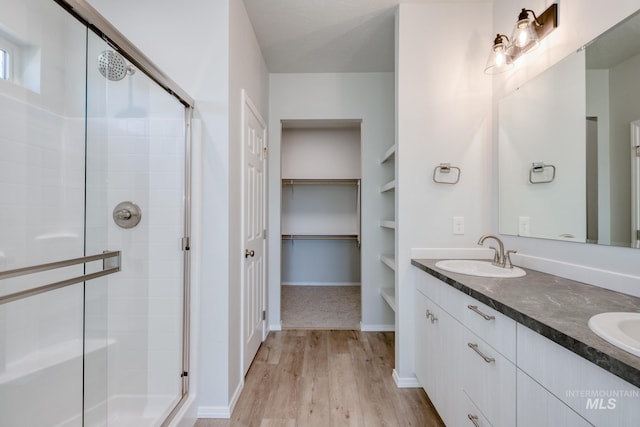 bathroom with a walk in closet, double vanity, a stall shower, wood finished floors, and a sink