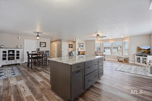 kitchen featuring light stone counters, a textured ceiling, dark hardwood / wood-style floors, and dark brown cabinetry