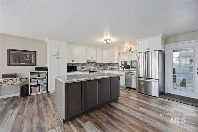 kitchen with light stone countertops, white cabinets, a center island, stainless steel appliances, and tasteful backsplash