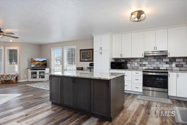 kitchen featuring white cabinets, a center island, decorative backsplash, stainless steel range with electric stovetop, and light stone counters