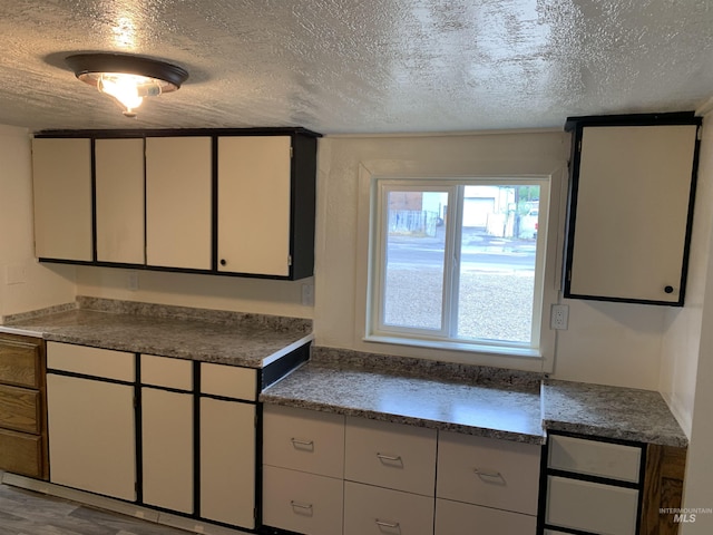 kitchen with white cabinets, a textured ceiling, and wood finished floors