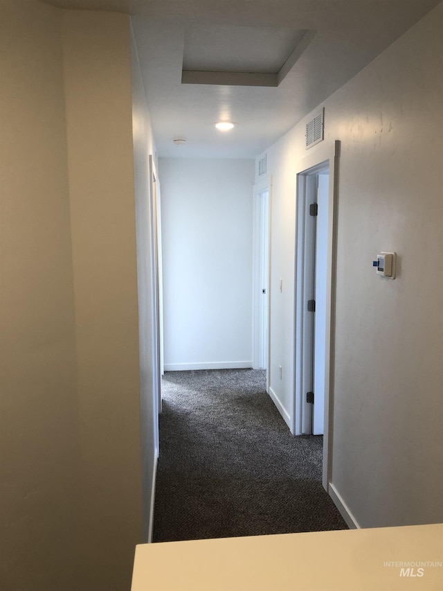 hallway with dark colored carpet and a tray ceiling