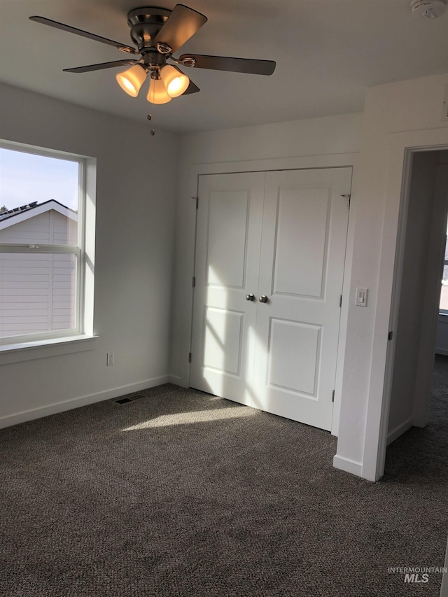 unfurnished bedroom with ceiling fan, a closet, and dark carpet