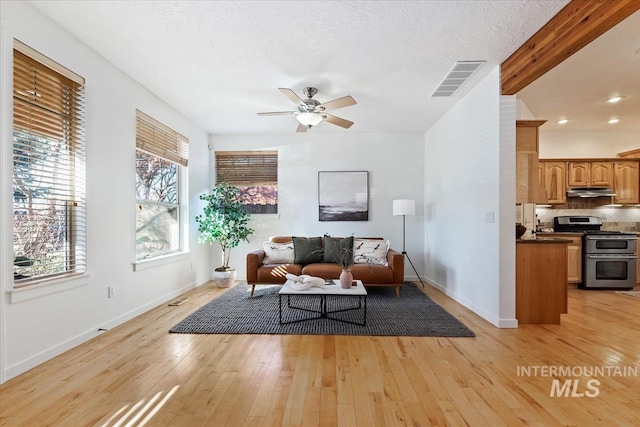 living area with light wood finished floors, visible vents, ceiling fan, a textured ceiling, and baseboards