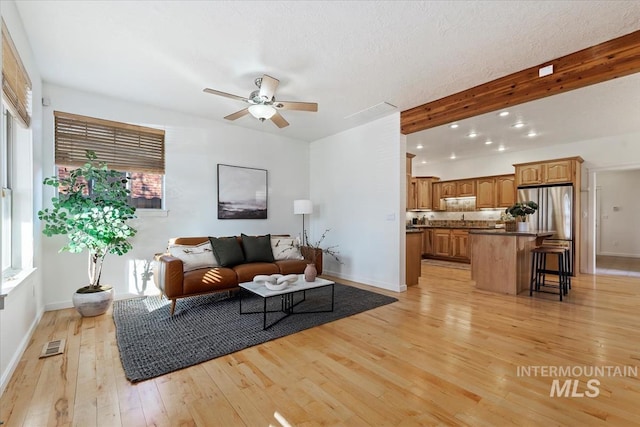 living room with beam ceiling, baseboards, visible vents, and light wood finished floors