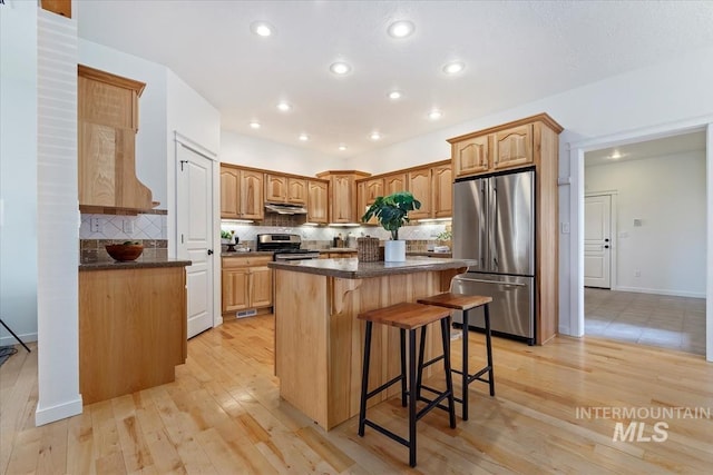 kitchen with a breakfast bar area, appliances with stainless steel finishes, a kitchen island, light wood-type flooring, and under cabinet range hood