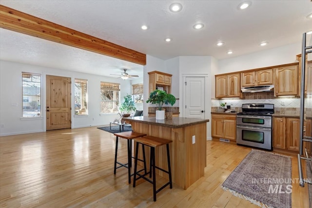 kitchen featuring range with two ovens, under cabinet range hood, a breakfast bar, a kitchen island, and backsplash