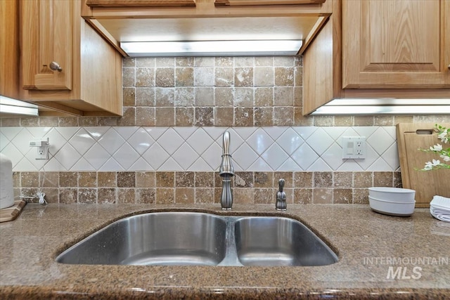 kitchen featuring dark stone counters, a sink, and decorative backsplash