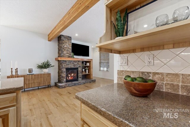 kitchen featuring tasteful backsplash, beamed ceiling, a textured ceiling, a stone fireplace, and light wood-style floors