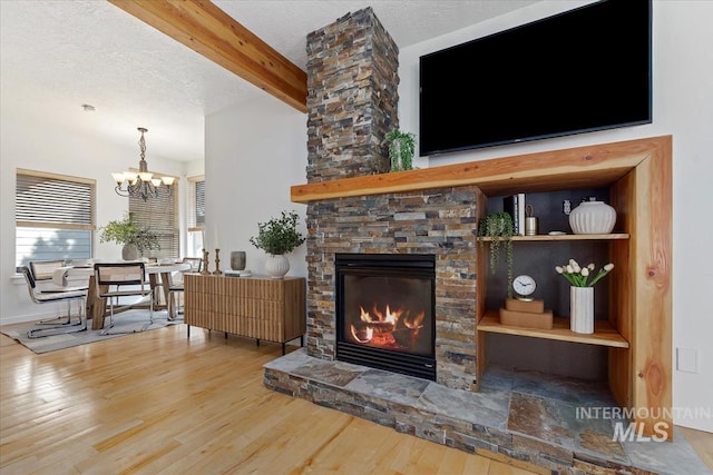 living room featuring a textured ceiling, beamed ceiling, a fireplace, and wood finished floors