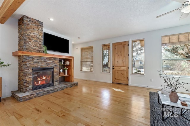 living room with a textured ceiling, a stone fireplace, wood finished floors, and a ceiling fan