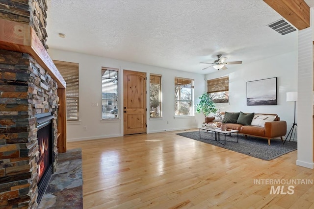 living room with ceiling fan, a textured ceiling, a stone fireplace, wood finished floors, and visible vents