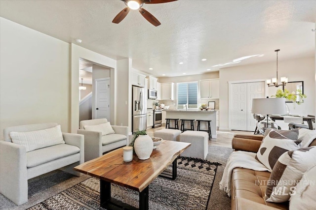 living room featuring ceiling fan with notable chandelier, light hardwood / wood-style floors, and a textured ceiling