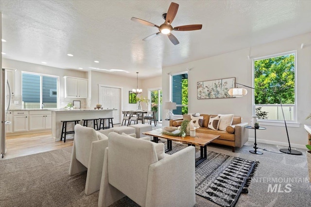 living room featuring ceiling fan with notable chandelier, a healthy amount of sunlight, and a textured ceiling